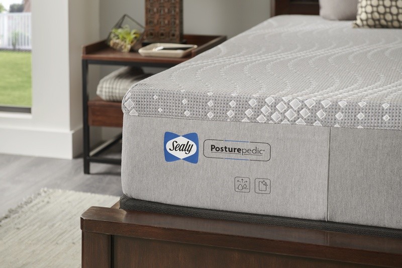 Closeup of grey Sealy Posturepedic mattress corner on a dark wood bed