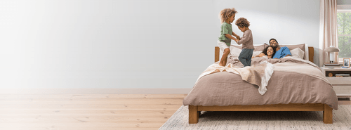 Couple laying on a dressed bed with children jumping