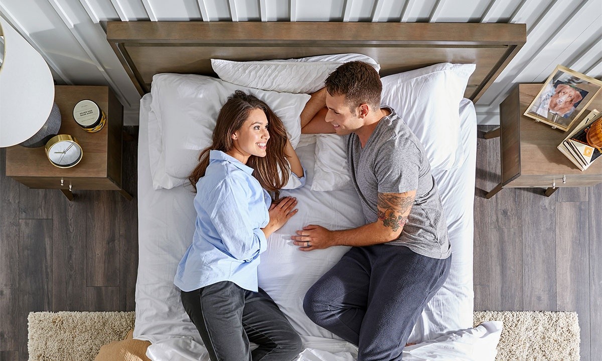 Man and woman laying in bed side by side looking at each other in bright room