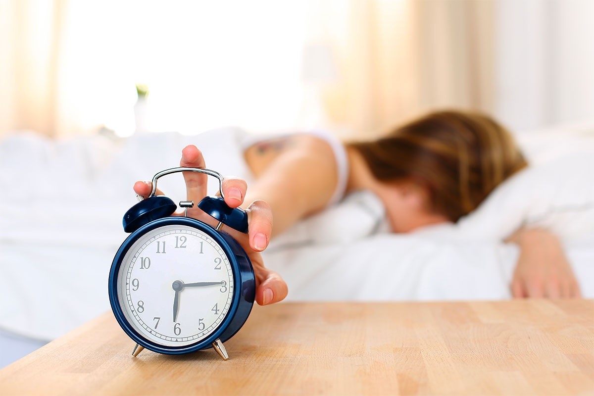 Tired woman turning off an alarm clock