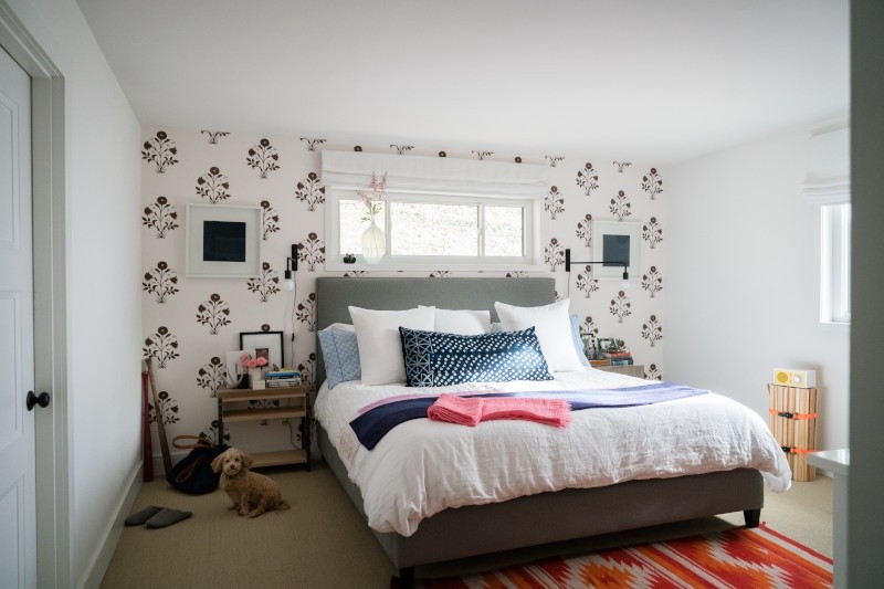 Open white bedroom with white flowered wallpaper and dog sitting on floor