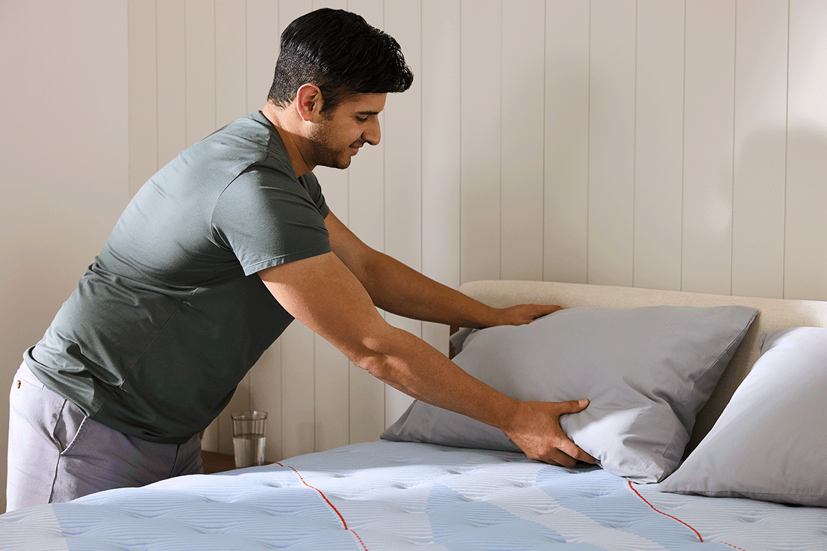 Man placing pillow on Posturepedic Plus Spring mattress