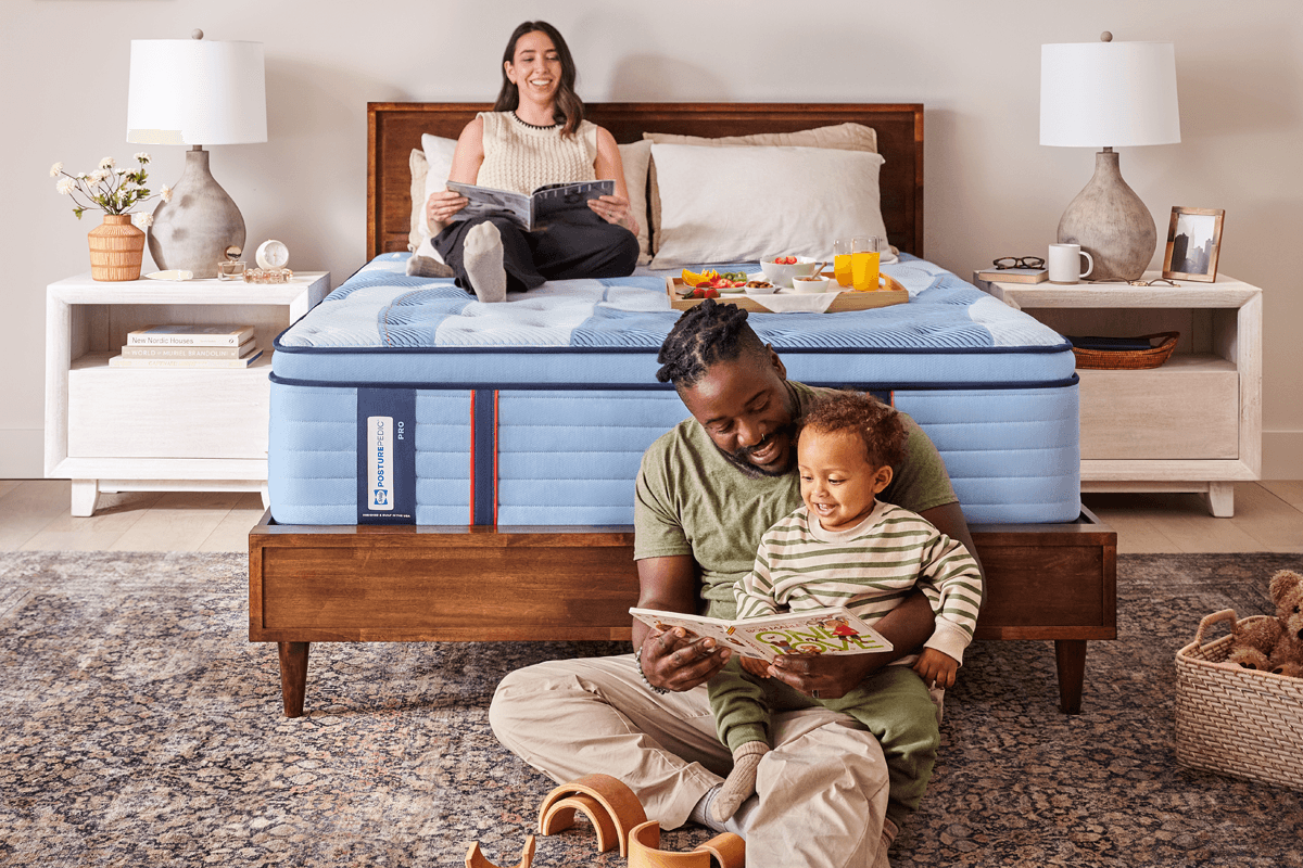 A father playing with a child while the mother reads in bed