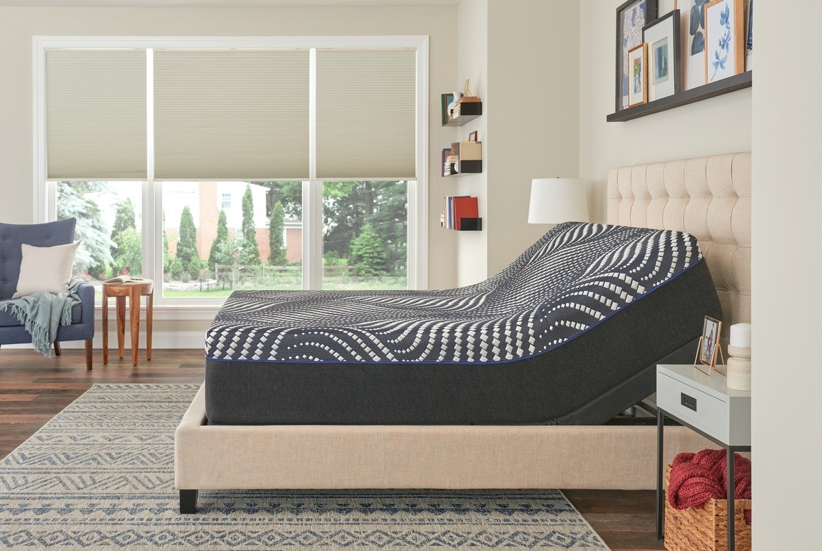 Sealy mattress on an adjustable base within a tan bed frame - in front of large windows and natural color decor