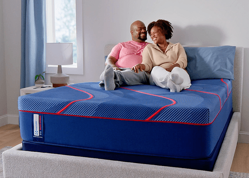 Man and woman laying on a Posturepedic Elite Hybrid mattress in a styled room