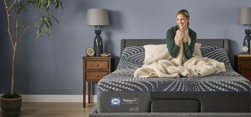 a blonde girl sitting on an adjustable posturepedic plus hybrid bed set with her blanket pulled into her